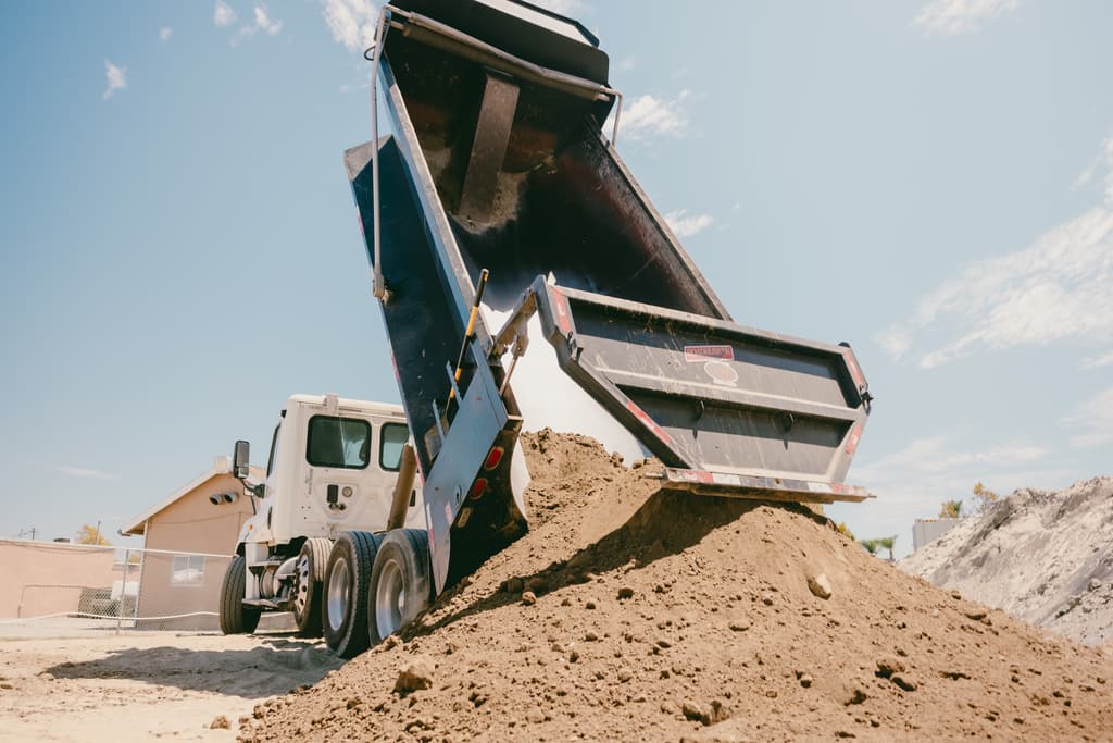 Dump truck with its bed fully raised unloading dirt onto the pile